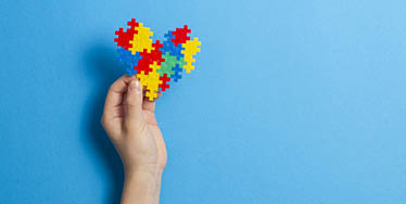 Kid hand holding multicolored heart on blue background  World autism awareness day concept