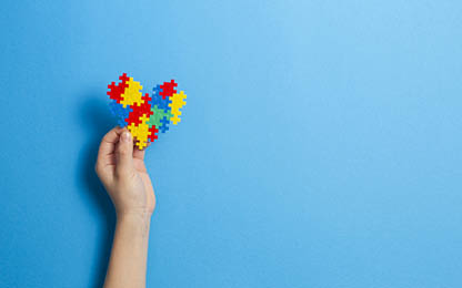 Kid hand holding multicolored heart on blue background  World autism awareness day concept