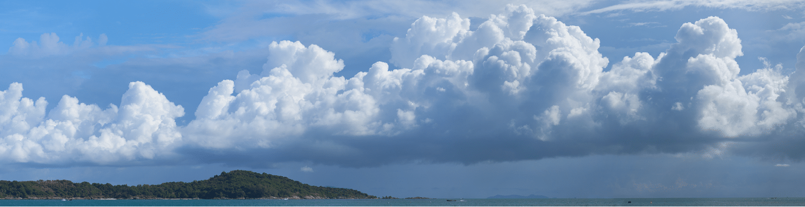 Beautiful panoramic photo of huge, billowing storm clouds, building and forming over the tropical sea near a popular tourist beach 