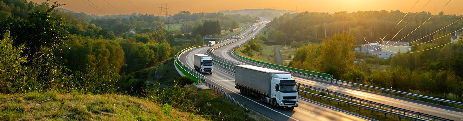 White trucks driving on the highway winding through forested landscape at sunset 