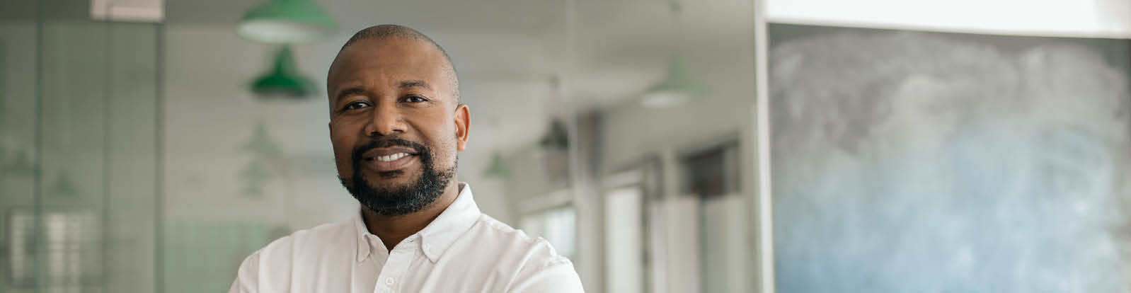 Portrait of a smiling mature African American businessman standing with his arms crossed in a large modern office in the late afternoon