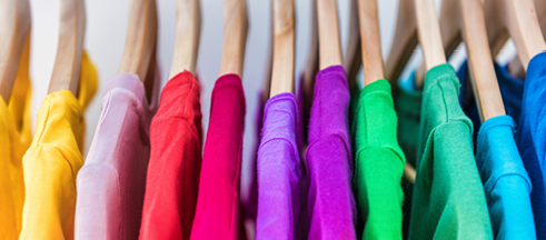 Fashion clothes on clothing rack - bright colorful closet  Closeup of rainbow color choice of trendy female wear on hangers in store closet or spring cleaning concept  Summer home wardrobe 