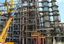 Construction and installation work with a powerful construction crane of a large new industrial oil refining petrochemical chemical plant with pipes, columns, railings, stairs and equipment 