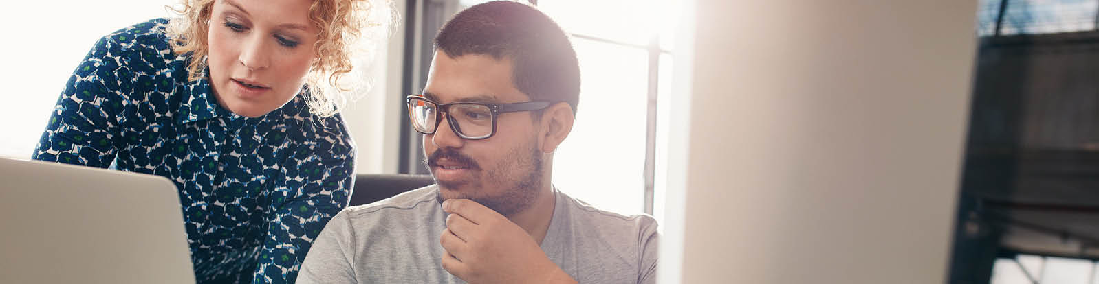 Shot of two designers working in their office using a laptop, digital graphics tablet and desktop computer  Man sitting at his desk with female colleague showing something on her laptop 