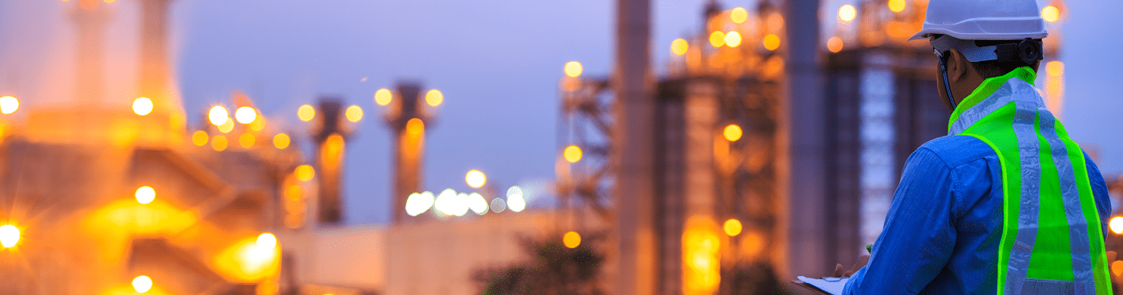 Worker with clipboard looking at oil refinery plant at sunrise